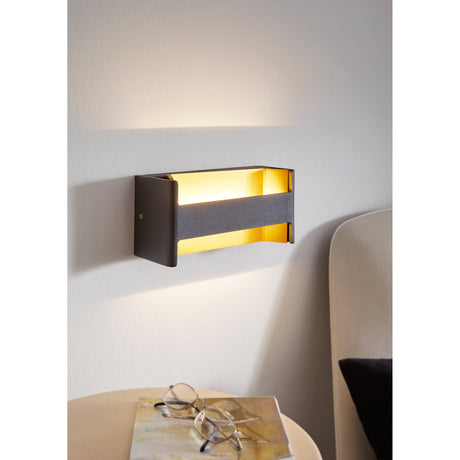Feloniche LED Wall Light in black and gold, rectangular aluminium body shown lit on a bedroom wall above a side table with glasses and a cushioned chair nearby.