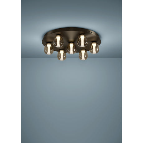 Ferro LED flush ceiling light in dark bronze, round steel plate with seven egg-shaped amber-tinted glass shades, mounted on a pale blue ceiling.