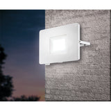 Fesvine LED Flood Light in white aluminium with recessed glass front, mounted on an exterior brick wall at dusk, illuminated with daylight white light.