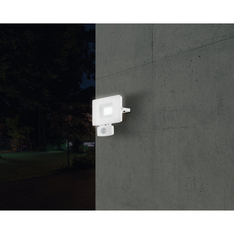 Fesvine LED flood light in white aluminium with glass front, wall-mounted with motion sensor beneath, illuminated at night against a concrete wall.