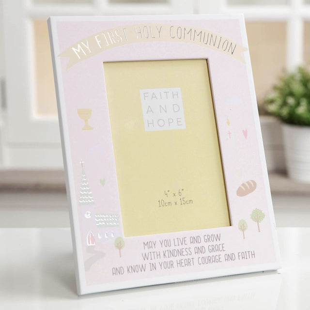 Pink wooden photo frame with "My First Holy Communion" banner, holding a 6 x 4in portrait photo, decorated with chalice, church, bread and tree illustrations, displayed on a table.