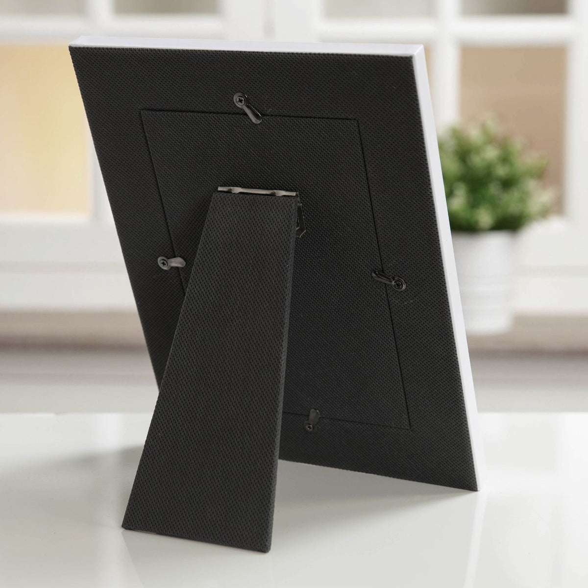 Back view of the My First Holy Communion wooden photo frame, 6 x 4in, showing a fabric-covered back panel with an adjustable kickstand and hanging hooks, displayed upright on a surface near a window.