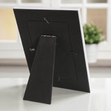 Back view of the My First Holy Communion wooden photo frame, 6 x 4in, showing a fabric-covered back panel with an adjustable kickstand and hanging hooks, displayed upright on a surface near a window.