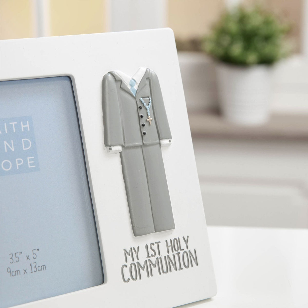 White resin photo frame for a 5 x 3.5in print, with a raised grey communion suit, rosary detail, and "MY 1ST HOLY COMMUNION" text, shown on a desk setting.