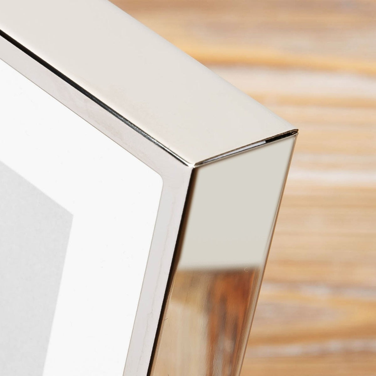 Close-up of the Confirmation Dove Metal Box Photo Frame 6 x 4in in Silver, showing the deep box edge and bright nickel-plated metal finish with a white mount, against a blurred wood background.