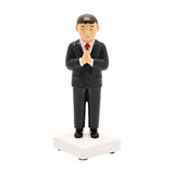 Resin Communion boy figurine with brown hair in a black suit, white shirt and red tie, hands pressed in prayer on a white square base, plain white background.