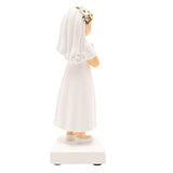 Communion girl figurine in resin, side view, showing dark brown hair under a white veil with floral crown, white dress, hands clasped in prayer, on a square white base against a plain background.