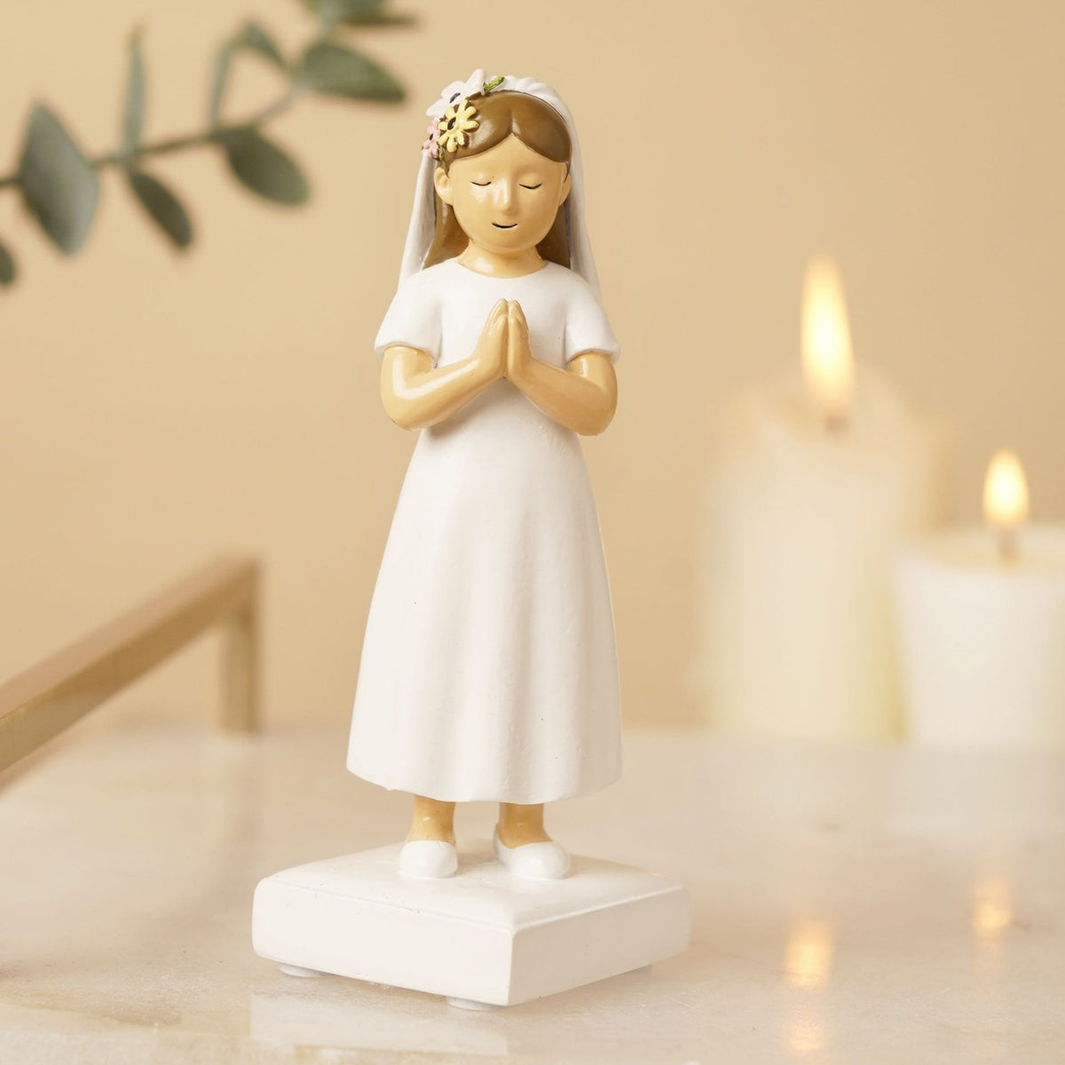 Resin Communion girl figurine with light brown hair, white dress and veil, hands pressed in prayer, on a white base, displayed near candles.
