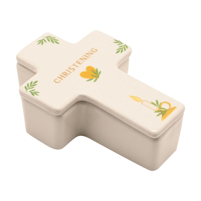 White ceramic cross-shaped trinket box with lid, printed "CHRISTENING" in gold, with green leaf and gold heart and candle motifs, on a plain white background.