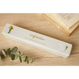 White ceramic rectangular Confirmation certificate keepsake box with gold cross and dove motifs, displayed on a wooden surface beside eucalyptus leaves and a book.