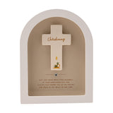 Arched white wooden plaque with a beige recess framing a cream cross inscribed "Christening" in gold script, a painted candle and leaves, and a small silver heart below, on a plain background.