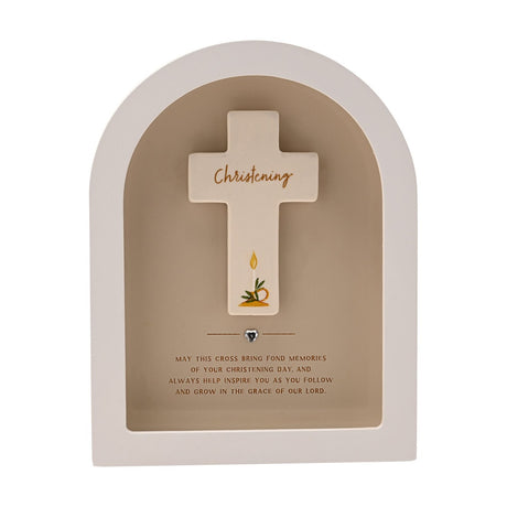 Arched white wooden plaque with a beige recess framing a cream cross inscribed "Christening" in gold script, a painted candle and leaves, and a small silver heart below, on a plain background.