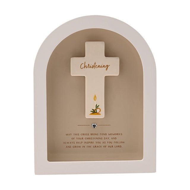 Arched white wooden plaque with a beige recess framing a cream cross inscribed "Christening" in gold script, a painted candle and leaves, and a small silver heart below, on a plain background.