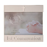 White enamel metal photo frame with silver trim, a small cross on the top bar and "1st Communion" lettering on the lower bar, holding a 4"x6" photo.