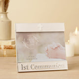 White enamel metal 1st Communion photo frame with silver trim, cross detail, and raised "1st Communion" lettering, shown landscape on a table with candles.