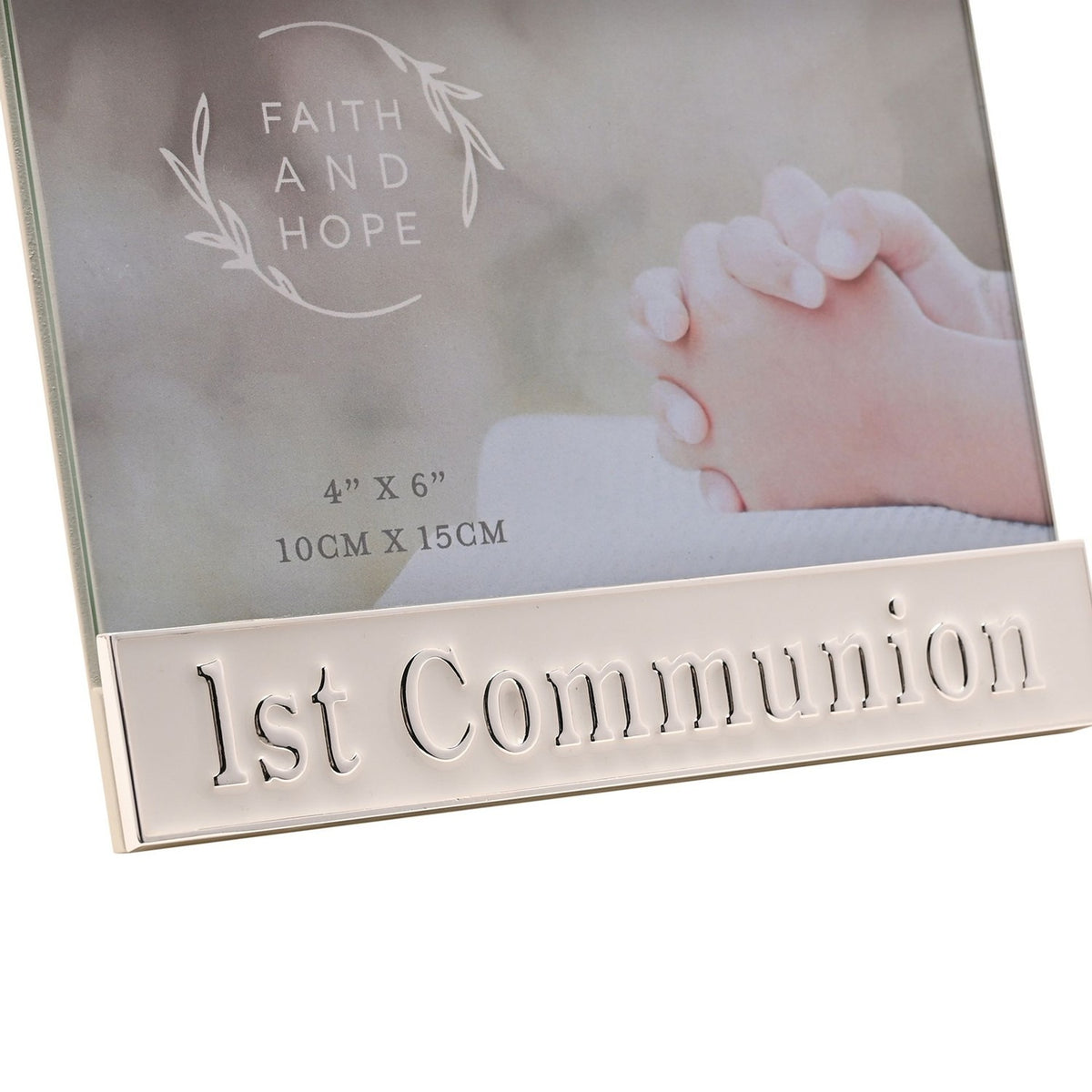 White enamel metal 1st Communion photo frame with silver trim, raised "1st Communion" lettering on the lower bar, holding a 4"x6" praying hands image.