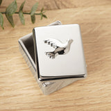 Rectangular Dove Confirmation metal keepsake box in polished silver, lid featuring a raised dove in flight, shown on a wooden surface with greenery nearby.