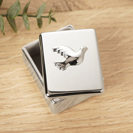 Rectangular Dove Confirmation metal keepsake box in polished silver, lid featuring a raised dove in flight, shown on a wooden surface with greenery nearby.