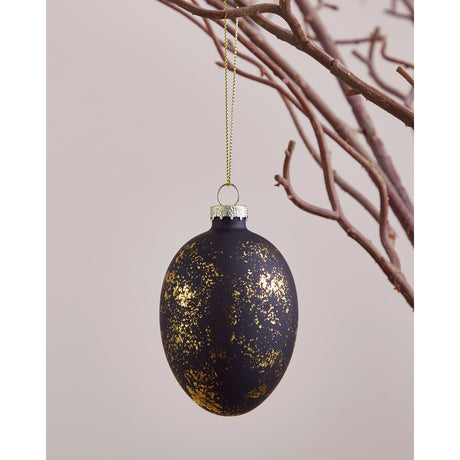 Fintry glass decorative egg in matt black with scattered gold flecks, silver-tone cap and gold hanging thread, shown against twigs on a light background.