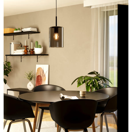 Firbora Smoked Glass Pendant Light 16cm in Black, a single-light cylindrical shade on a black cord with visible bulb, shown over a dining table in a living space.