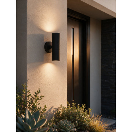 Firvette 2 Light Outdoor Wall Light in black, fluted aluminium cylinder on a round wall plate, mounted beside a front door and casting light upward and downward.