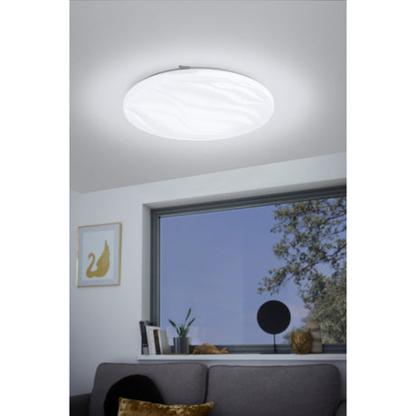 Fismenne LED flush ceiling light, 44cm round white diffuser with a wave texture pattern, mounted on a living room ceiling above a grey sofa near a window.