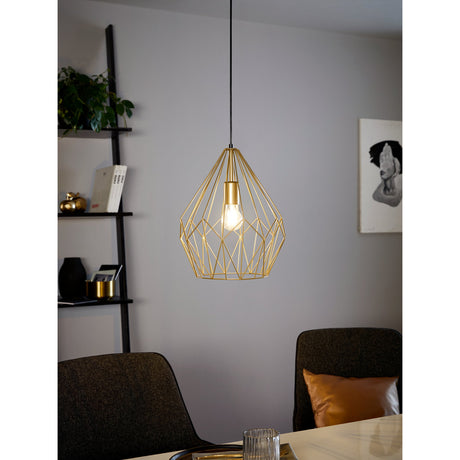 Flermanne Pendant Light 31cm in gold, an open geometric steel wire cage with E27 bulb, hung from a black cord above a dining table in a living space.