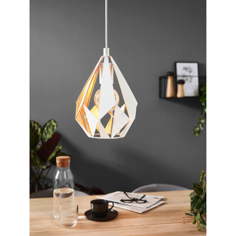 Flermanne Pendant Light in white and gold steel with a faceted teardrop shade and exposed bulb, shown hanging above a wooden dining table in a dark grey room.