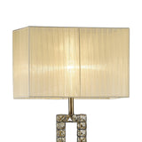 A close-up of the Florence Rectangle 1 Light Crystal Floor Lamp, featuring a brass stem with stacked glass squares and a rectangular cream pleated shade.