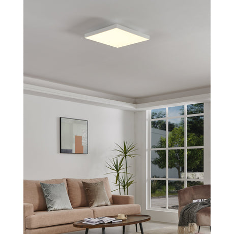 Flornorne square LED ceiling panel light, 45 x 45cm, white finish, illuminated on a living room ceiling above a sofa and armchair.