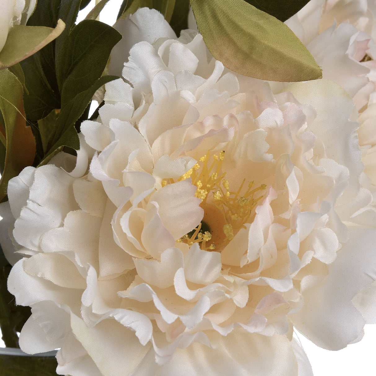 Close-up of the Hill Interiors White Fashion Peony faux flower, showing ruffled white petals, yellow stamens and green foliage.
