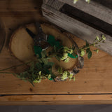 Hill Interiors Green Wild Meadow Rose faux stem with ruffled blooms and leaves, resting on a birch wood slice beside green-handled secateurs.