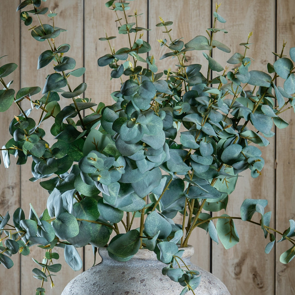 Hill Interiors Variegated Eucalyptus faux stems arranged in a stone vase, displaying rounded green leaves against a pale wooden plank background.