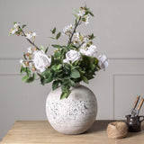 Hill Interiors Eucalyptus Filler arranged with white roses and blossom branches in a speckled stone ball vase on a wooden table.