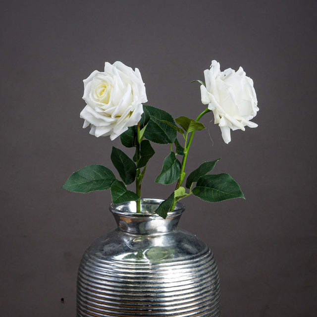 Large white garden rose faux stems by Hill Interiors in a ribbed silver vase, showing full blooms and green leaves against a grey backdrop.