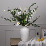 Hill Interiors Large Cineraria Eucalyptus Spray arranged with white blooms in a stone vase on a wooden console beside lemons and a framed photo.