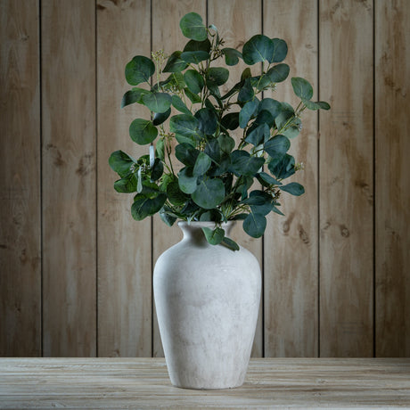 Hill Interiors Eucalyptus Stem Spray with silvery-green rounded leaves arranged in a pale stone vase on a wooden table against a wood plank background.