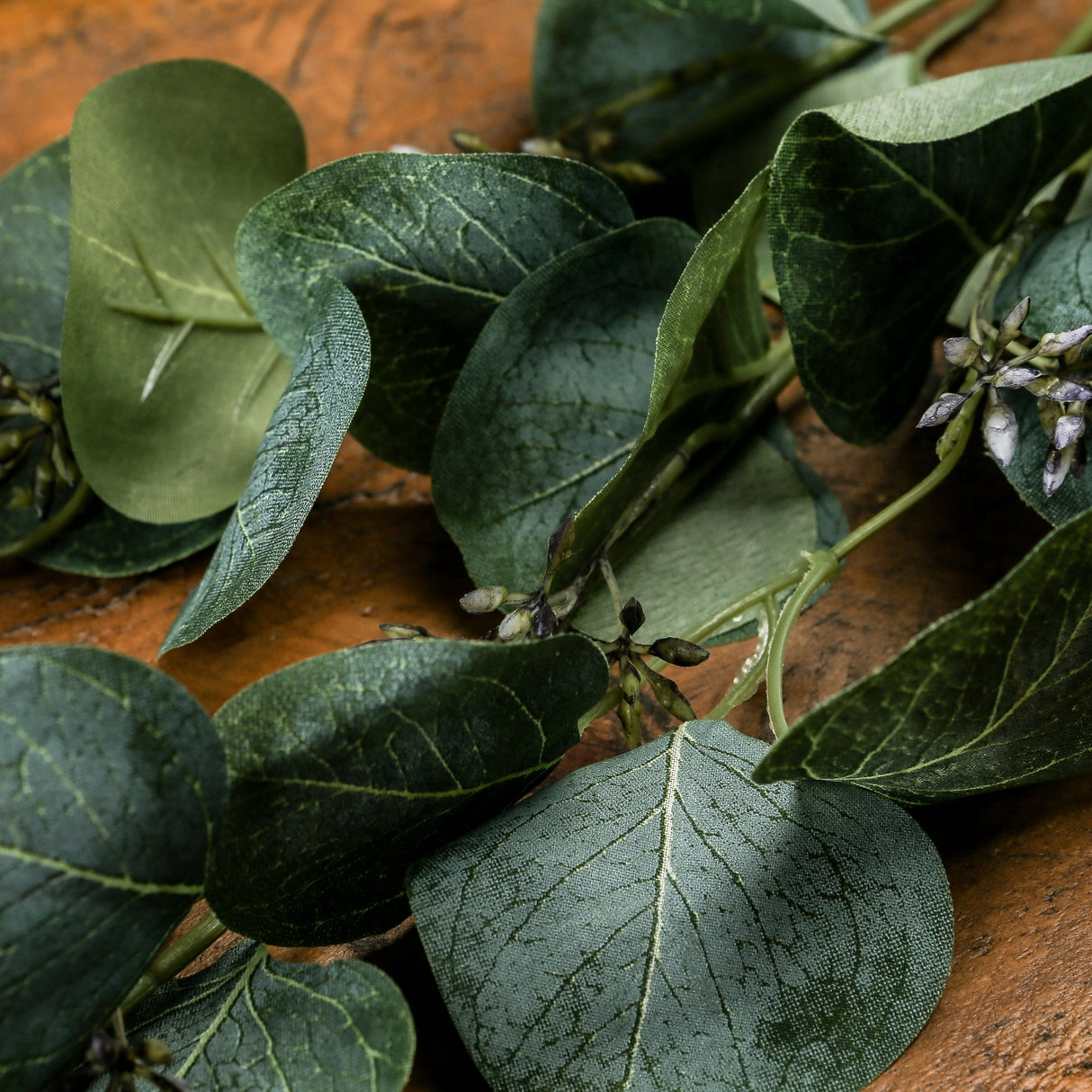 Hill Interiors Eucalyptus Stem Spray with rounded green plastic leaves and small budded clusters trailing across a warm wooden surface.