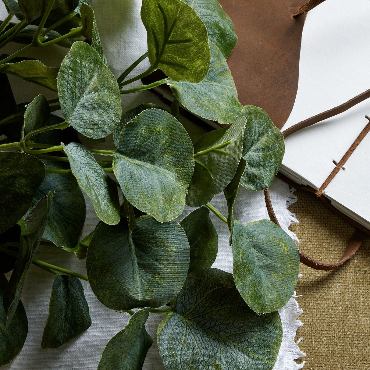 Hill Interiors Short Eucalyptus Bunch with rounded silvery-green plastic leaves, styled on white linen beside a leather-bound journal.