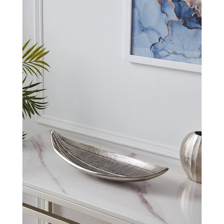 Forleyet Decorative Bowl in antique nickel aluminium, leaf-shaped with embossed rib detailing and upturned ends, displayed on a marble console table in a living room setting.