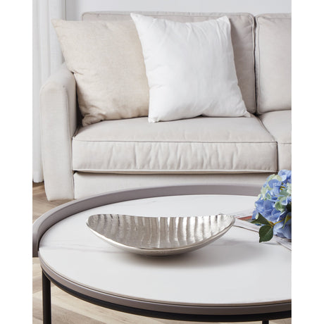 Forleyet Decorative Bowl in nickel aluminium with a ribbed, shell-like shape, styled on a coffee table beside a beige sofa with white and natural cushions.