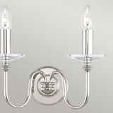 The Finsbury Park 2 Light Wall Light in polished nickel highlights a vintage-inspired charm with its two candle-shaped bulbs set on a sleek, curved metallic base and accompanied by a circular backplate against a neutral backdrop.