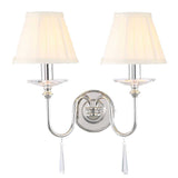 The Finsbury Park 2 Light Wall Light in polished nickel boasts two white lampshades and elegantly curved arms. Each arm is adorned with crystal pendants, offering a sophisticated touch to this vintage-inspired lighting fixture.