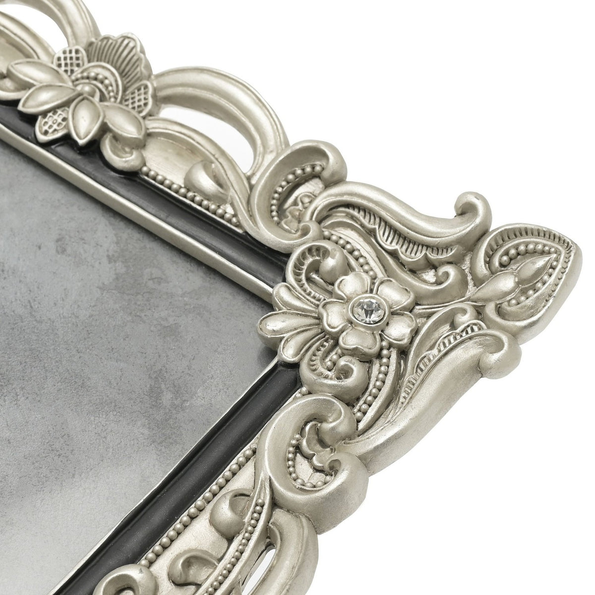 Close-up of an antique-style silver resin photo frame corner, showing scrollwork, a crystal-set flower detail and slim black inner edge against a white background.