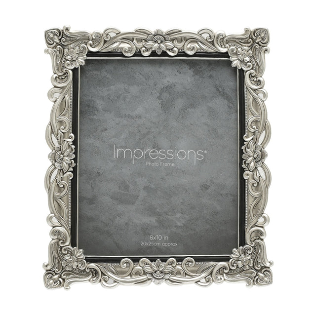 Rectangular resin photo frame in silver with raised floral scrollwork and crystal accents at the corners, holding a grey sample print for 8x10in photos on a white background.