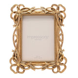 Gold resin photo frame with openwork bowknot corners, beaded border, and easel back, holding a 5x7in photo, shown on a white background.