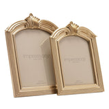 Two winged arch photo frames in champagne resin with ridged leaf crests and reeded side mouldings, 5x7in and 4x6in sizes, on a white background.