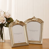 Two Winged Arch resin photo frames in champagne finish with arched crest tops and reeded mouldings, shown on a wooden surface beside white roses.