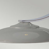Close-up of a dome-shaped light fixture in a glossy gray finish. This elegant Franklin Desk Lamp - Grey, mounted on a gracefully curved metal arm against a soft light gray background, exemplifies modern style. The directed task lighting highlights a small emblem on the surface of the fixture.