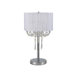 The Freida 3 Light Crystal Table Lamp features a polished chrome frame, cylindrical white shade, and hanging crystal accents for a modern touch.